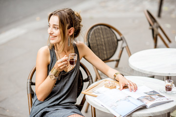Young stylish woman in gray dress drinking coffee outdoors at the cafe in Paris