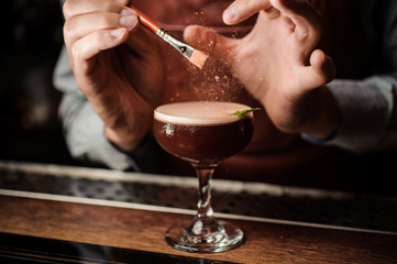 The barman decorates the cocktail with a gold powder. Magic image