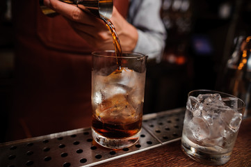 barman hand pouring drink from measuring cup into cocktail glass filled