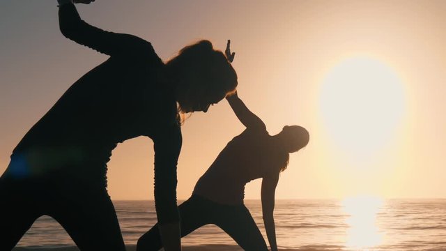 Group of 3 women practicing yoga on the beach against the sunset. Three black silhouettes of their bodies making yoga postures. Sun and the ocean creates ethereal & pure scene