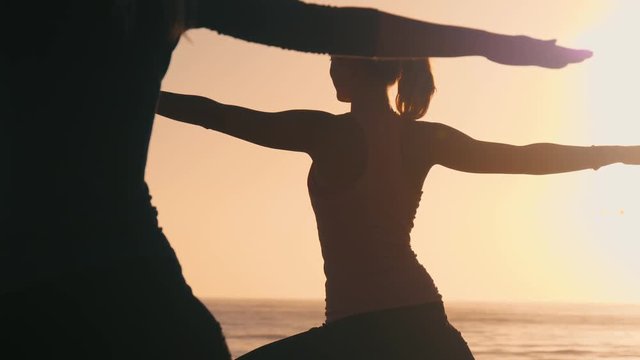 Group of 3 women practicing yoga on the beach against the sunset. Three black silhouettes of their bodies making yoga postures. Sun and the ocean creates ethereal & pure scene