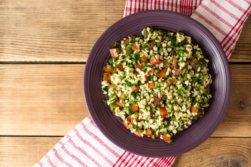 Tabbouleh salad with bulgur, tomatoes, parsley, green onion and mint in plate on wooden table.