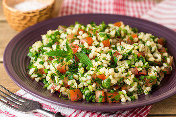 Tabbouleh salad with bulgur, tomatoes, parsley, green onion and mint in plate on wooden table.