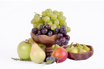 Light and dark grapes in a wooden bowl with an apple pear plum and figs on a white background.Fruit still life