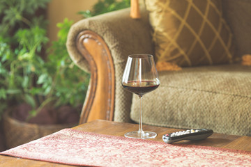 A glass of red wine on a coffee table with tv remote