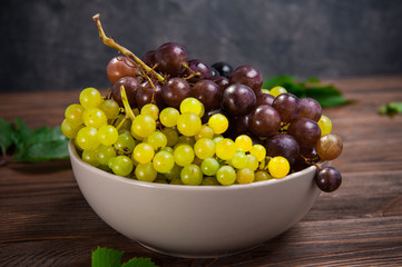 Close up bowl of various grapes: red, white and black berries on the dark wooden table. Selective focus.