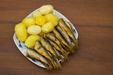 Fried baltic herring with boiled potatoes on a plate on wooden background
