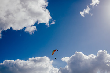 .Photograph of extreme sport. Image of people flying on paragliding on a sunny and somewhat cloudy day with a blue background in summer. Lifestyle picture.