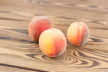 Three fresh whole ripe peaches on old rustic wooden planks