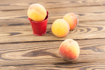 One fresh whole ripe peach in red metal bucket and three peaches separately on rustic old wooden planks