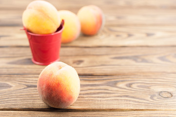 One fresh whole ripe peach in red metal bucket and three peaches separately on rustic old wooden planks