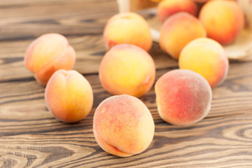 Lot of fresh whole ripe peaches poured out of wicker basket on rustic old wooden planks