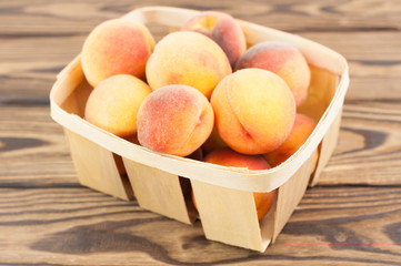 Lot of fresh whole ripe peaches in wicker basket on rustic old wooden planks