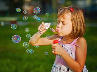 Cute little girl biowing soap bubbles.
