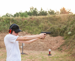 Handsome young policeman agent aiming and shooting at a target with a pistol  desert eagle gun wearing black hat and white shirt in nature ambient firing firearms bullets in the air training