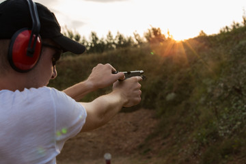 Caucasian handsome young policeman or special force army soldier changing bullets in the gun  pistol aiming to shoot at distant target practicing in nature wild outside with firearms.