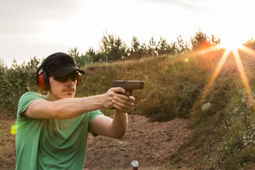Profile of a young handsome policeman during training in the battlefield outside of the city ready to take criminals and shooting with the gun  pistol at the target professional in the nature