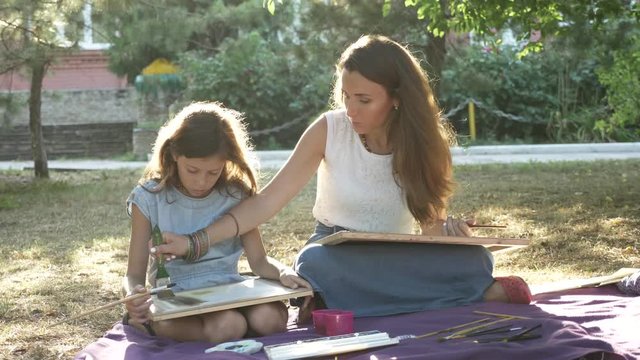 Woman with daughter drawing by watercolor paints at the park