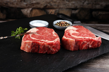 Raw fresh meat Ribeye Steak, seasoning and meat fork on dark background