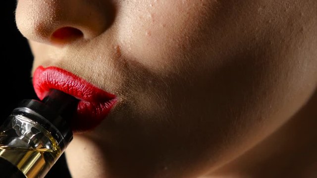 Girl smokes a wipe, her lips have red lipstick. Black background. Close up