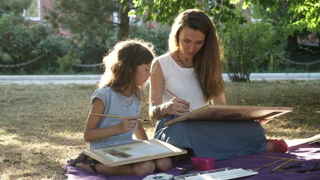 Woman with daughter drawing by watercolor paints at the park