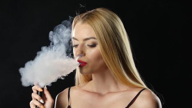 Girl smokes an electronic cigarette in a dark room. Black background
