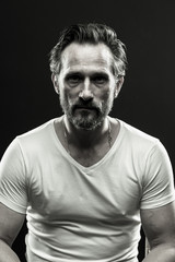 Black and white portrait of brutal beardy man. Monochrome photo of mid aged male on black backdrop.