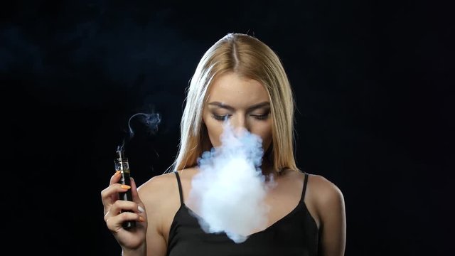 Blonde in a spacious room smokes an electronic cigarette. Black background