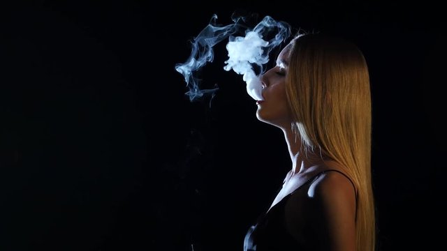 Girl of extraordinary beauty smokes an electronic cigarette. Black background. Side viwe