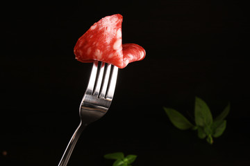 Salami Spain sausage Salchichon on a fork on a dark black background