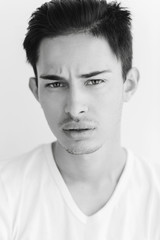 Portrait of a young man with dark hair and light eyes. on a white background. The guy in the white T-shirt. Male model. Black and white portrait of a young man