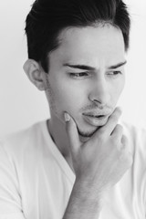 Fototapeta premium Portrait of a young man with dark hair and light eyes. on a white background. The guy in the white T-shirt. Male model. Black and white portrait of a young man