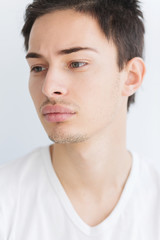 Obraz premium Portrait of a young man with dark hair and light eyes. on a white background. The guy in the white T-shirt. Male model.