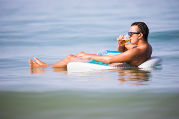 Man relax in the ocean water on rubber ring drink beer and enjoy summer vocation.