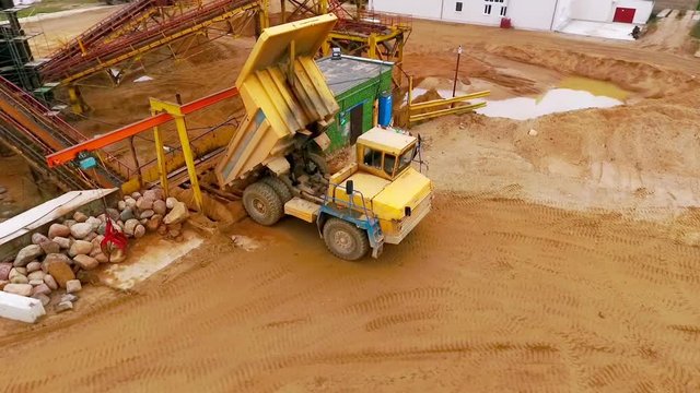 Dump truck dumping sand to sorting conveyor. Sand sorting process on mining conveyor. Aerial view of mining machinery working at sand quarry. Mining equipment for sorting sand. Mining truck