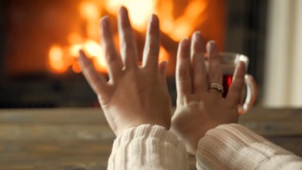 4k footage of young woman warming her hands in living room at fireplace