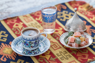 Turkish coffee with glass of water and turkish delights on traditional table cloth