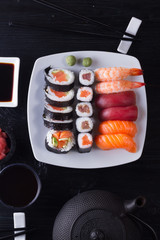 Japanese sushi with teapot and tea cups on dark black wooden background, top view
