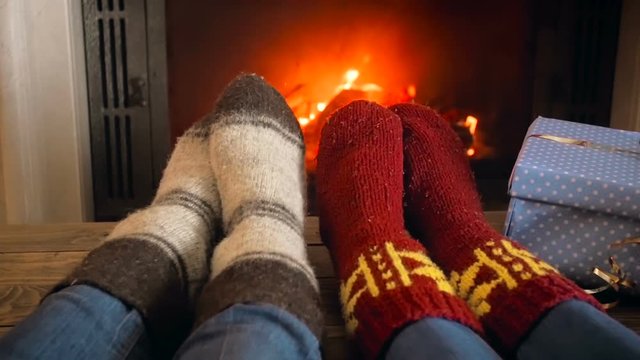 Closeup video of couple in woolen socks relaxing by the fireplace next to heat of Christmas gifts