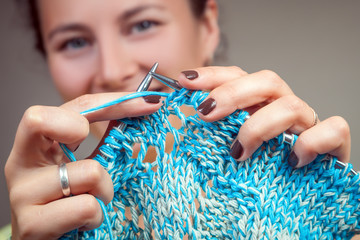 A young dark-haired married woman smiling and pointing at the camera as knit from natural woolen threads a white and blue striped sweater. A close-up of an example of how to properly knit