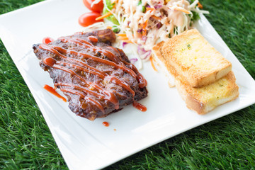 Close up view of pork barbecue ribs with barbecue sauce that served with garlic bread and vegetable salad.