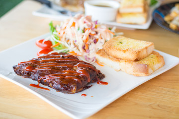Close up view of pork barbecue ribs with barbecue sauce that served with garlic bread and vegetable salad.