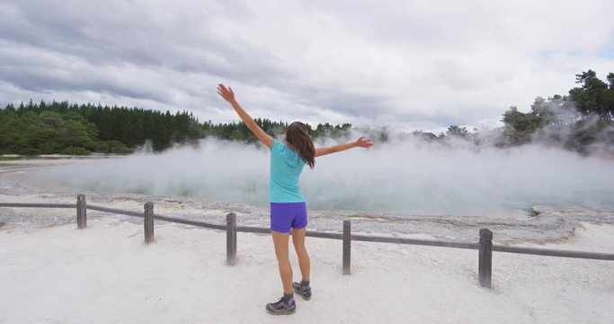 New Zealand happy tourist woman jumping happy having fun at famous attraction travel destination. Champagne pool, Waiotapu. Active geothermal area, in Taupo Volcanic Zone, Rotorua, New Zealand.