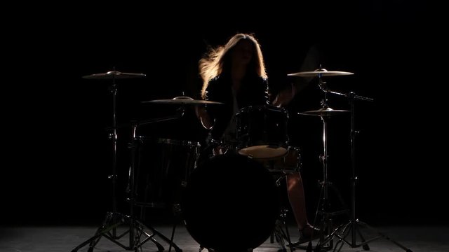Girl is kicks from playing drums, playing energetic music. Black background. Silhouette