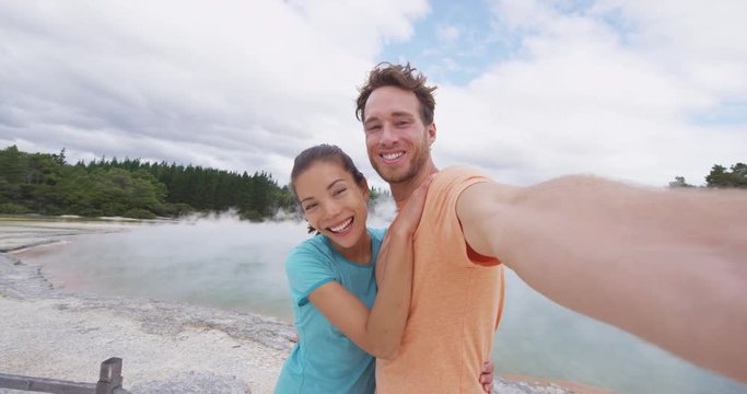 Tourists couple taking selfie at New Zealand Waiotapu pools travel destination. Young people having fun sightseeing at colorful geothermal hot springs ponds, Waiotapu, Rotorua, New Zealand.