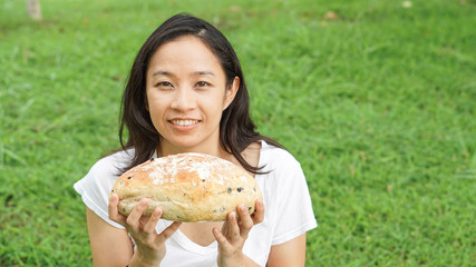 Asian woman holding and eating fresh baked bakery in green background park