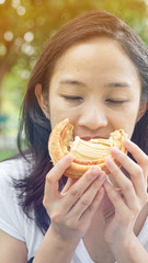 Asian woman holding and eating fresh baked bakery in green background park