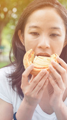 Asian woman holding and eating fresh baked bakery in green background park