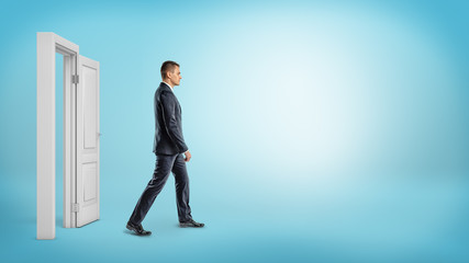 A businessman on blue background walking through an open white doorframe. © gearstd