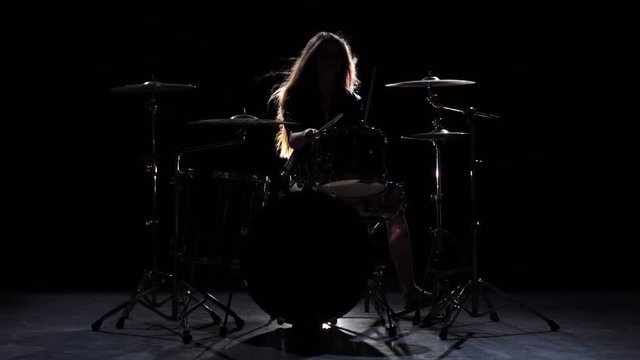 Girl is kicks from playing drums, playing energetic music. Black background. Silhouette. Slow motion